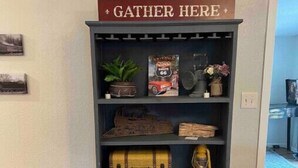 A bookshelf with a 'GATHER HERE' sign, vintage Route 66 memorabilia, a lantern, and a wooden chest. - HUGE house across st from GC railway- hot tub (Williams)