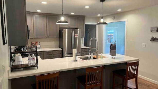 A modern kitchen with a central island, stainless steel appliances, pendant lighting, and wooden chairs. - HUGE house across st from GC railway- hot tub (Williams)