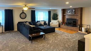 A living room with a sectional sofa, a coffee table, a fireplace, and a clock on the wall. - HUGE house across st from GC railway- hot tub (Williams)