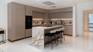 A modern kitchen with marble countertops, built-in appliances, and bar stools.