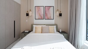 A modern hotel bedroom with a large bed, two bedside tables, a nightstand, a wardrobe, and two abstract paintings on the wall.