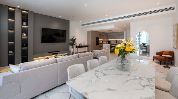 A modern living room with a large sectional sofa, a marble coffee table, and a flat-screen TV mounted on the wall.