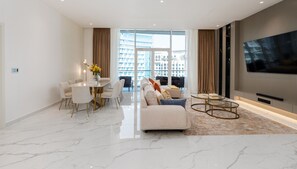 A modern living room with a dining area, large windows, and a flat-screen TV.