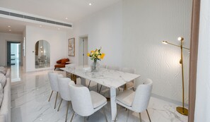 A modern dining room with a marble table, grey upholstered chairs, and a vase of yellow flowers.