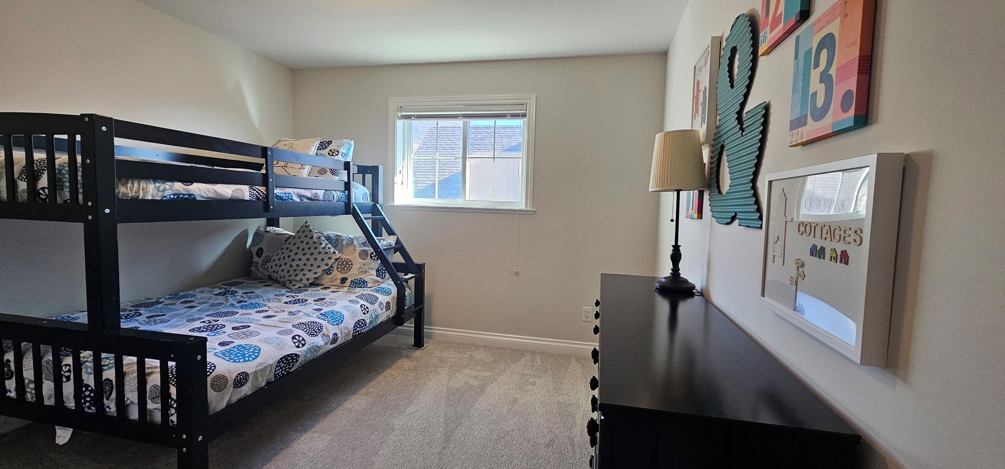 A bunk bed room with a window, a desk with a lamp, and wall decorations.
