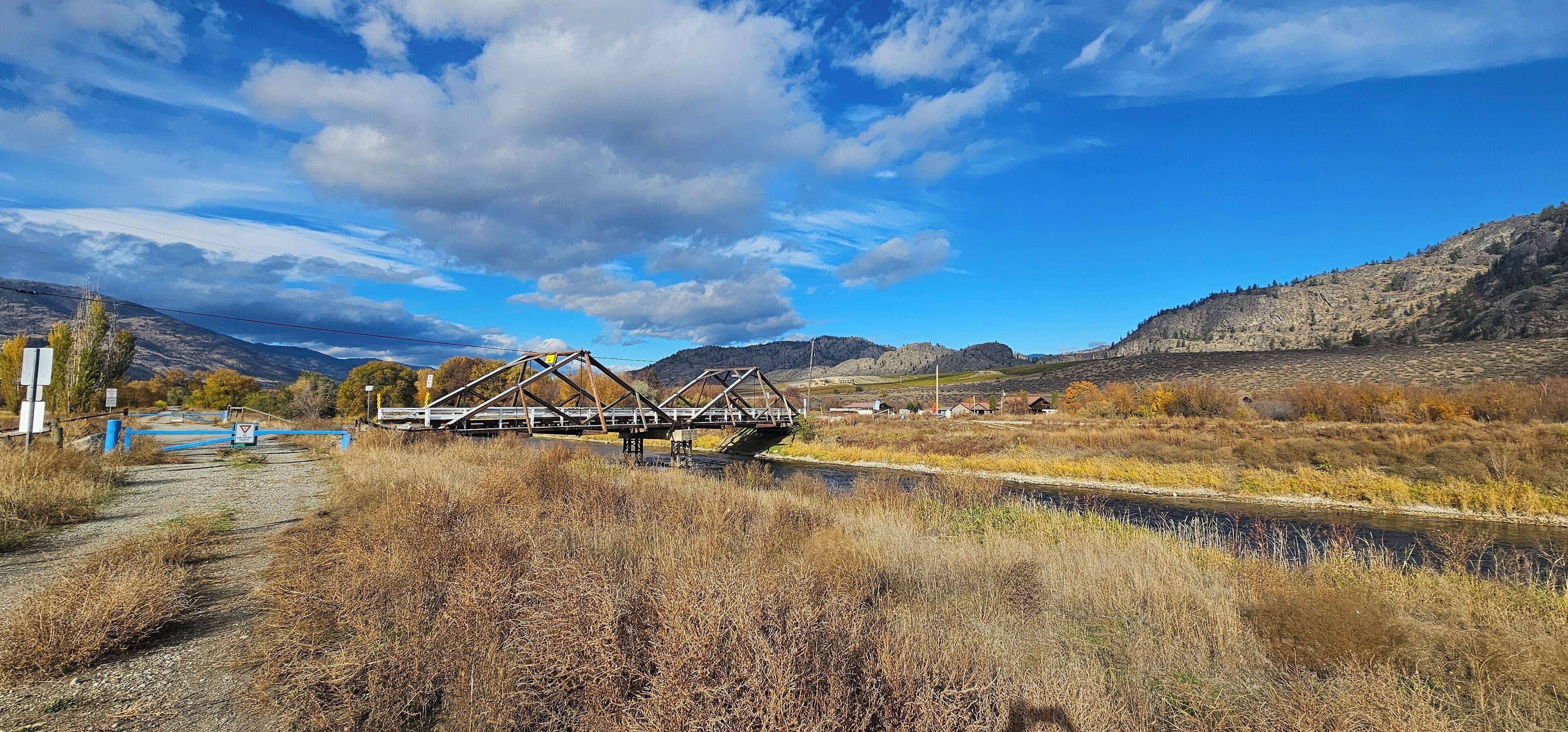 A metal bridge over a river with a clear sky and mountains in the background.