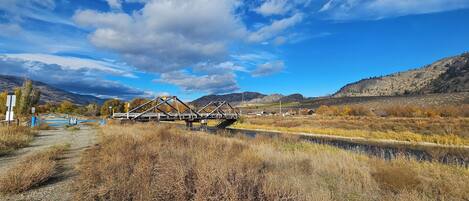 A metal bridge over a river with a clear sky and mountains in the background.
