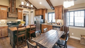 A spacious kitchen with wooden cabinets, a large island with seating, a built-in oven, and a stainless steel refrigerator. - Aspenwood Manor (Provo)