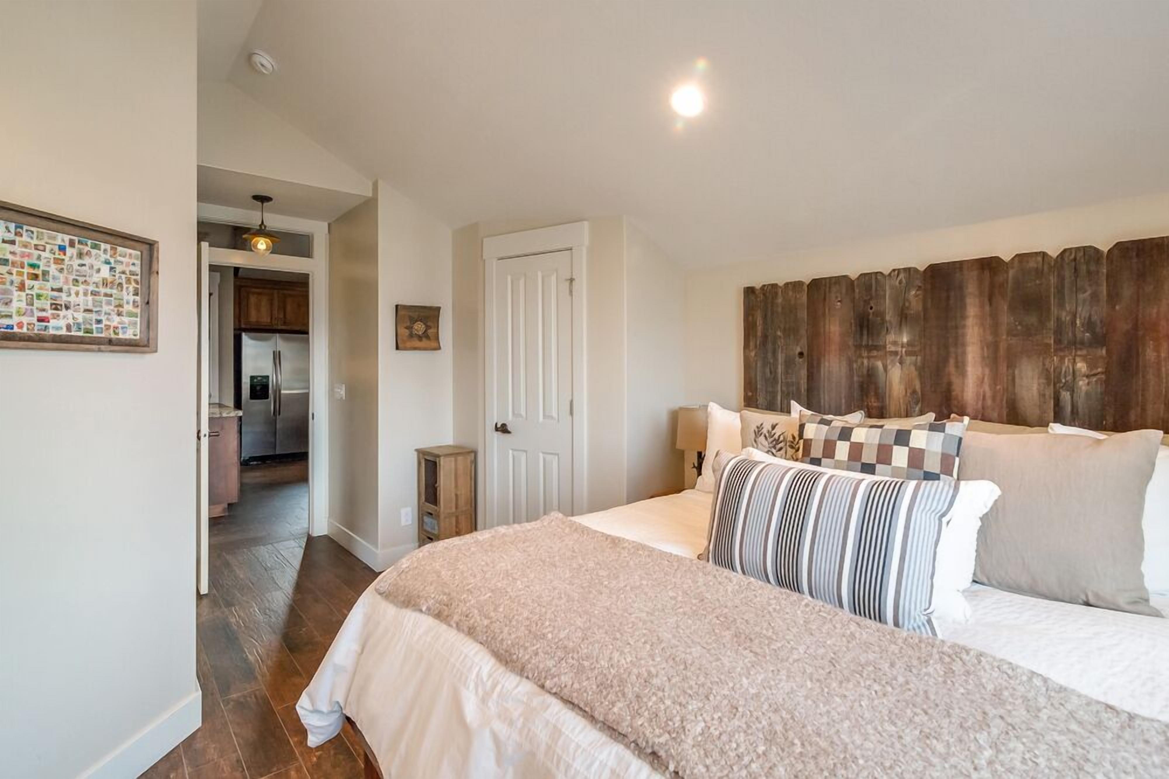 A bedroom with a large bed, a wooden headboard, and a view into the kitchen.
