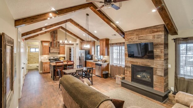 A spacious living area with a fireplace, wooden beams, and a ceiling fan. - Aspenwood Manor (Provo)