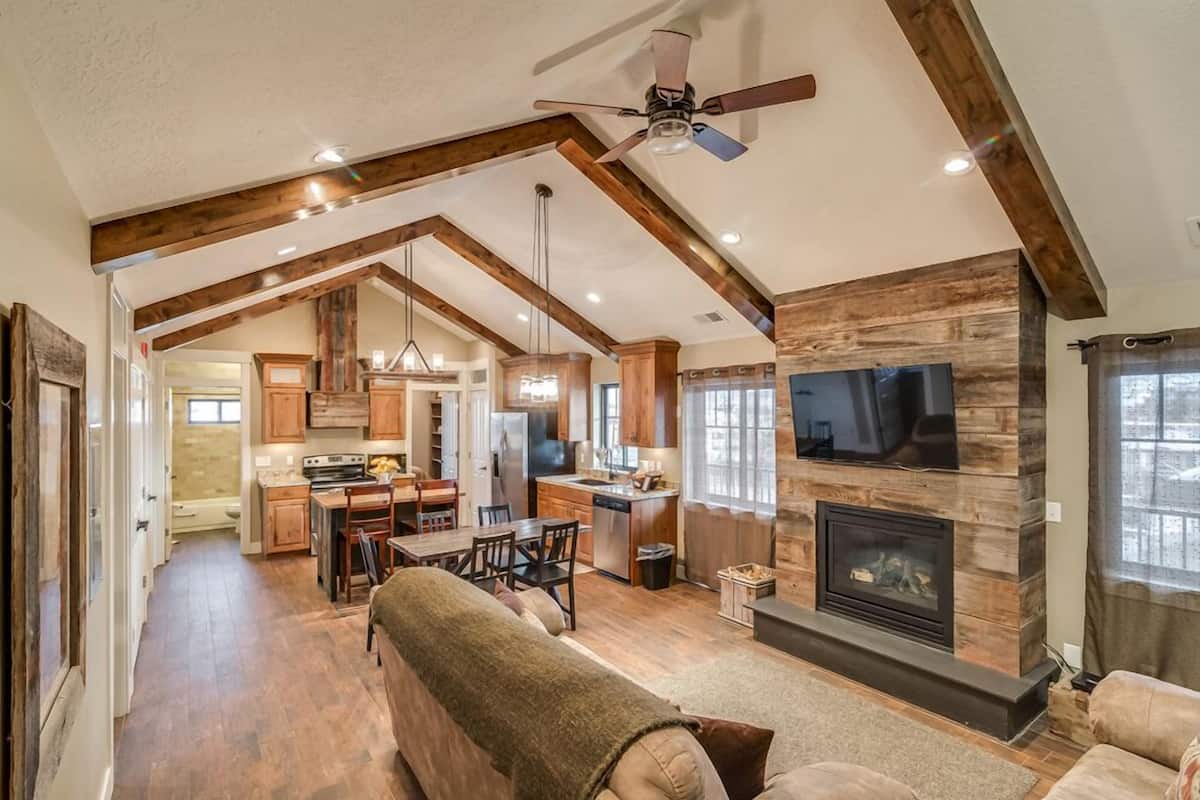 A spacious living area with a fireplace, wooden beams, and a ceiling fan.