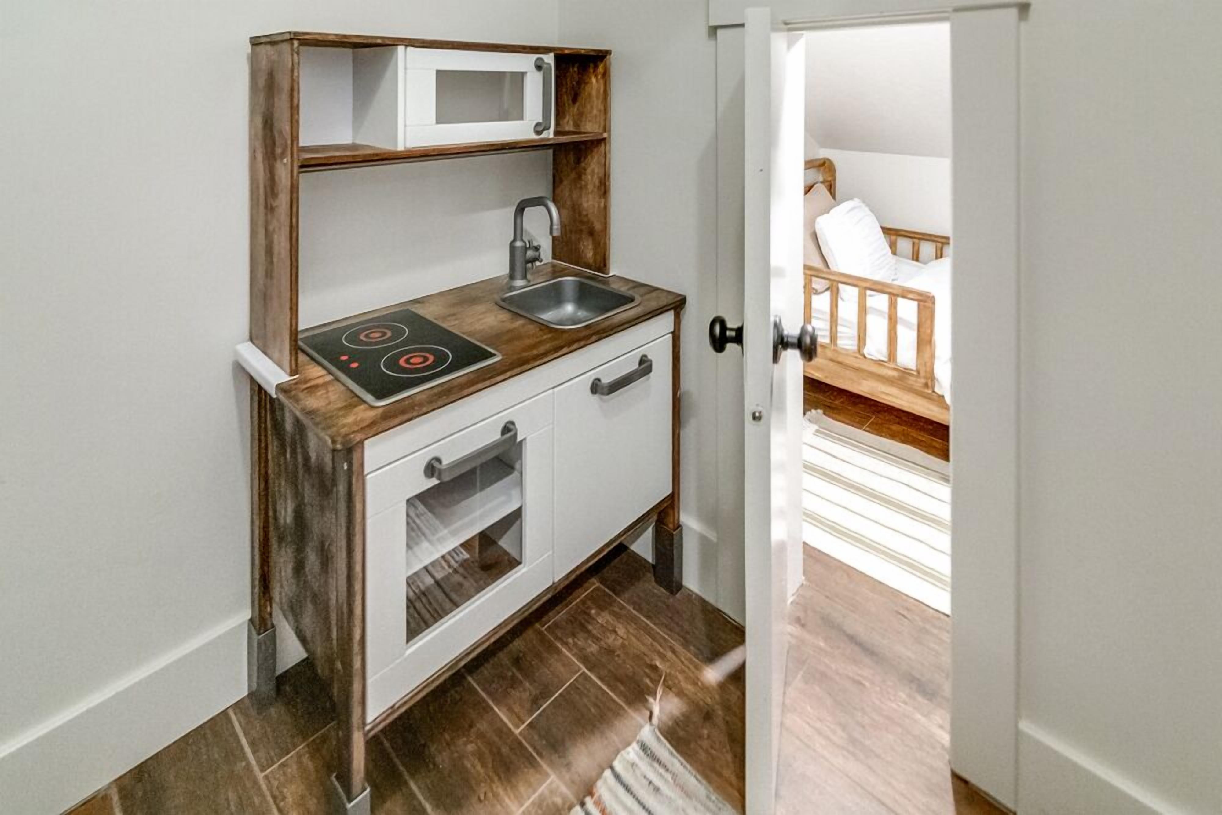 A compact kitchenette with a microwave, sink, and stove, leading to a bedroom with a wooden bed and white bedding.