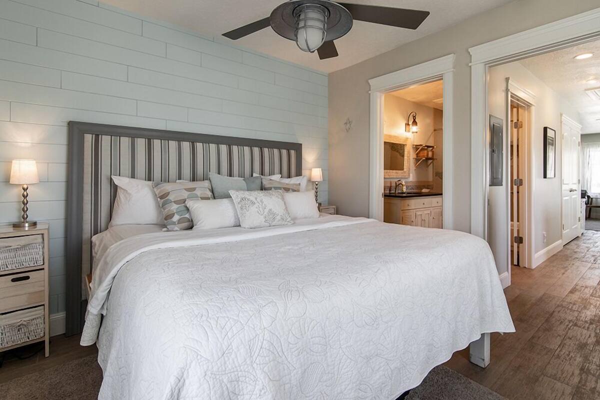 A bedroom with a large bed, a ceiling fan, and a nightstand with a lamp.