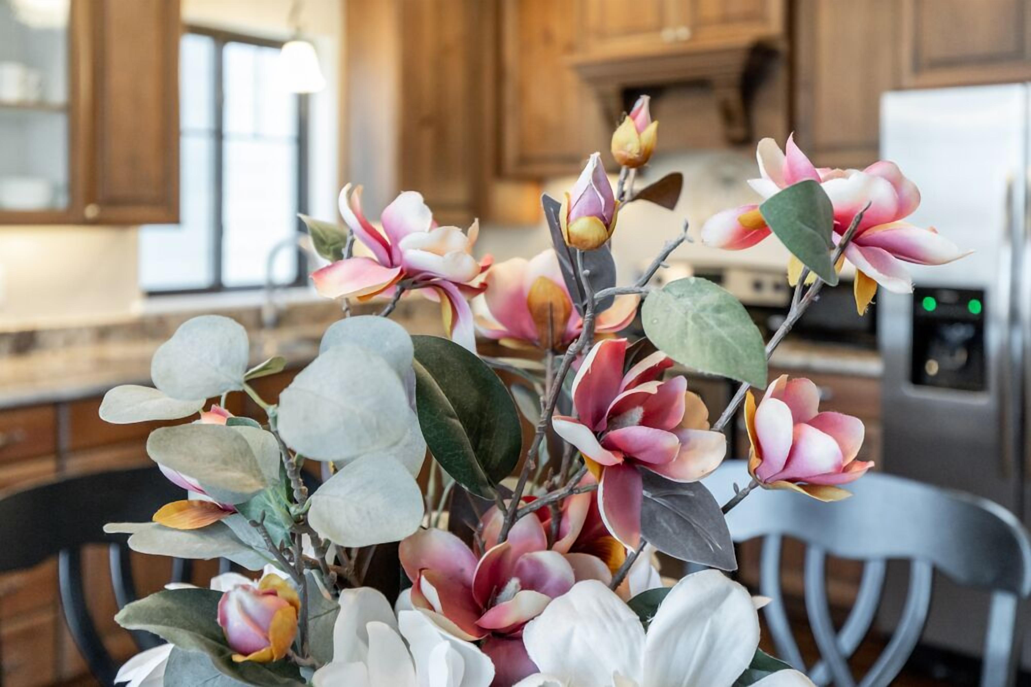 Uma cozinha com armários de madeira, uma geladeira de aço inoxidável e um vaso com flores artificiais.