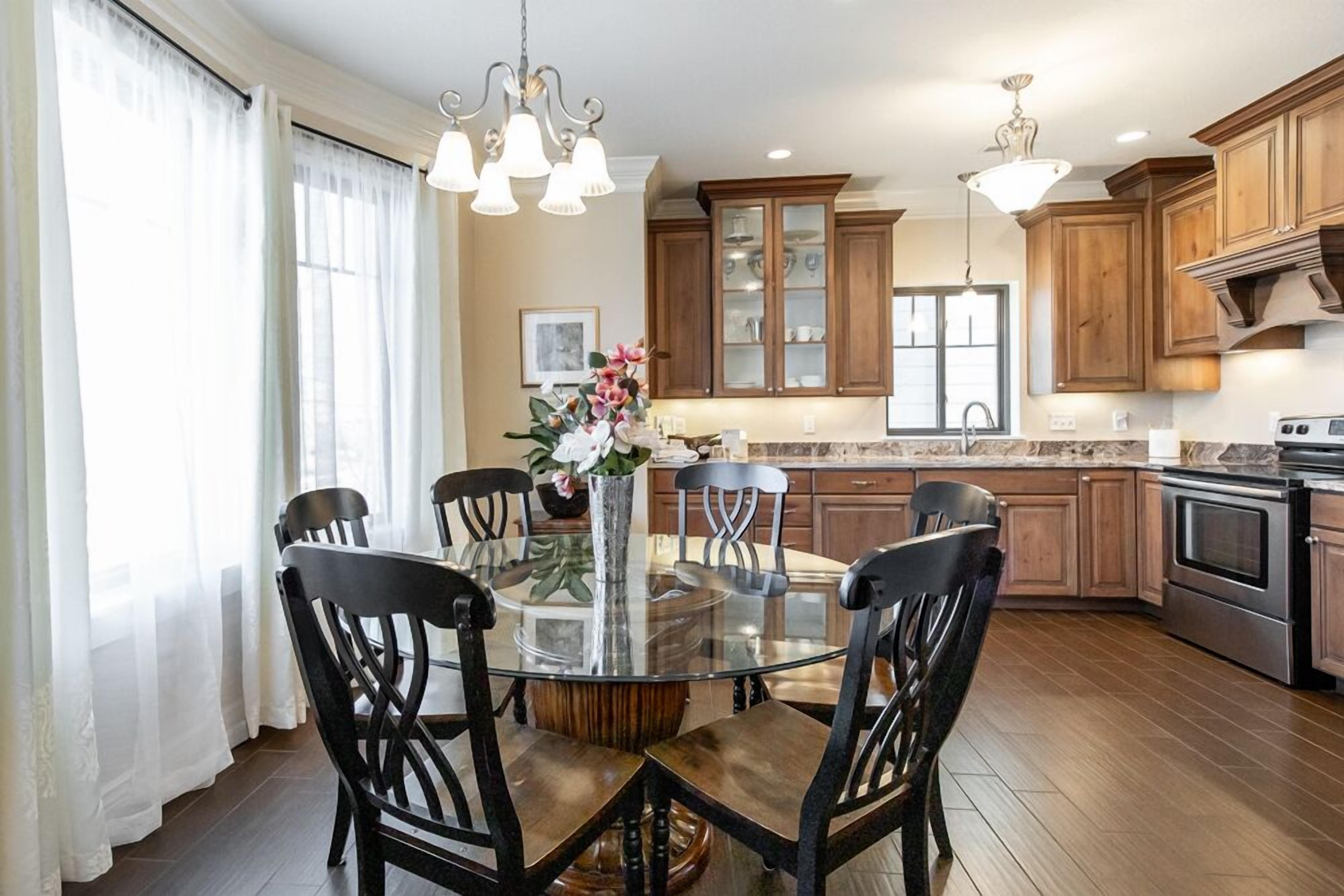 Un comedor con una mesa redonda de vidrio rodeada de sillas, armarios de madera y una cocina al fondo.
