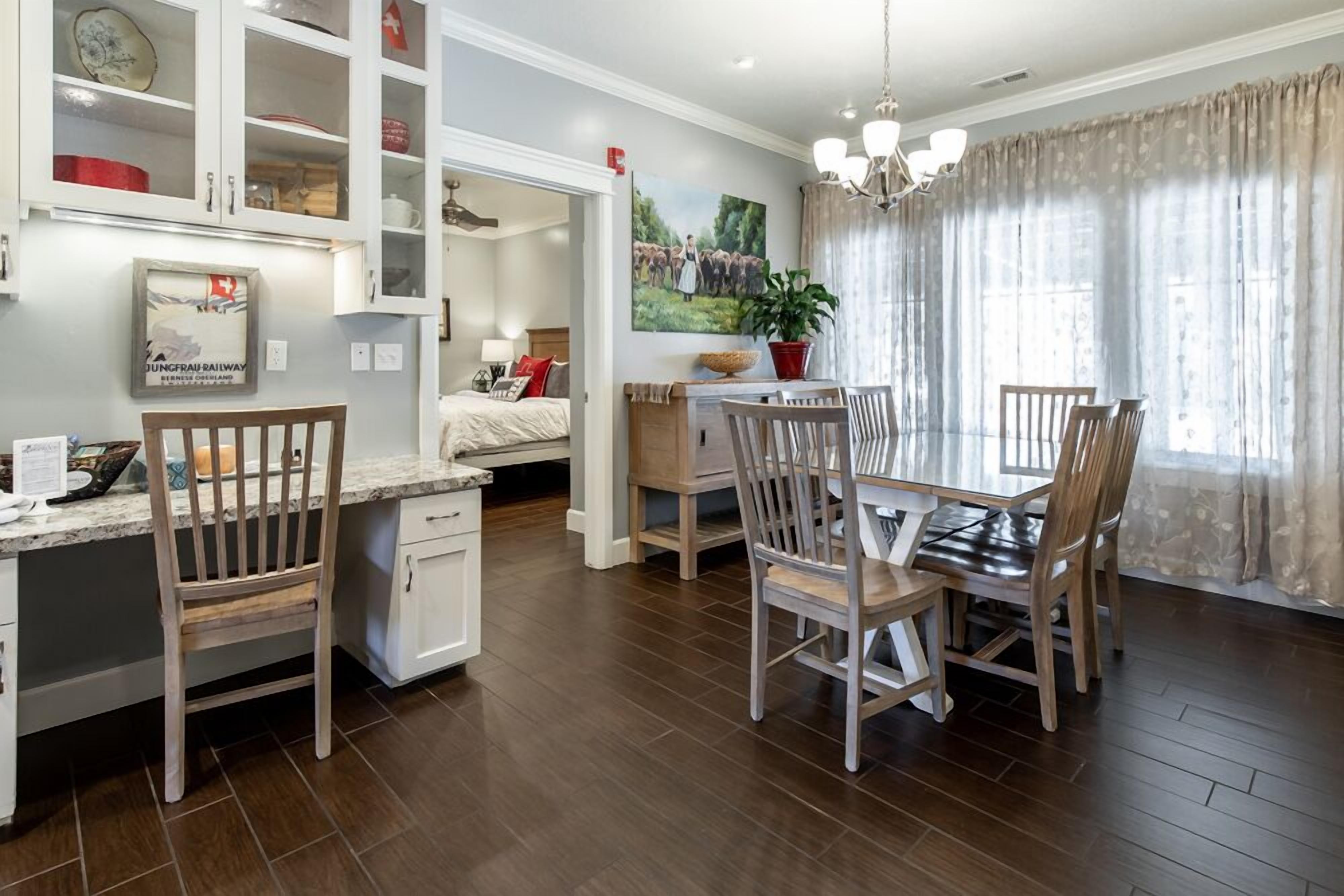 A modern kitchen with wooden cabinets, a dining area with a table and chairs, and a large window with curtains.