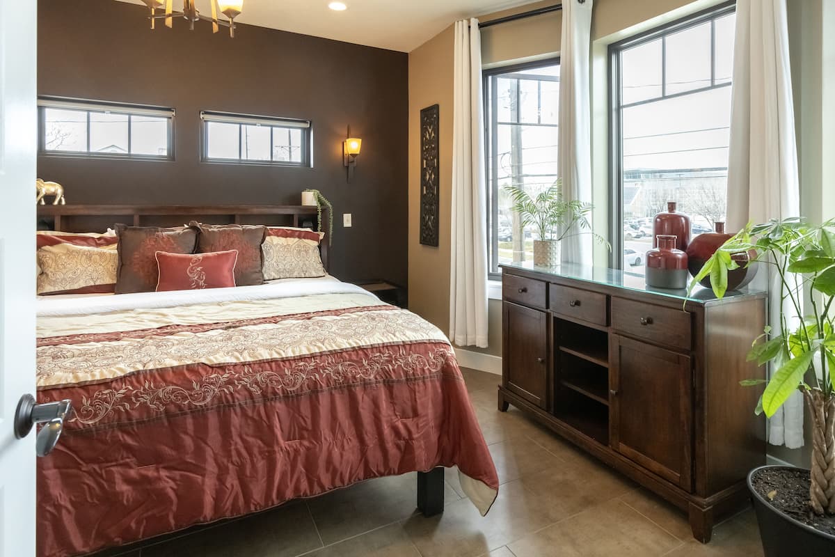 A bedroom with a large bed, a wooden dresser, and a window with curtains.