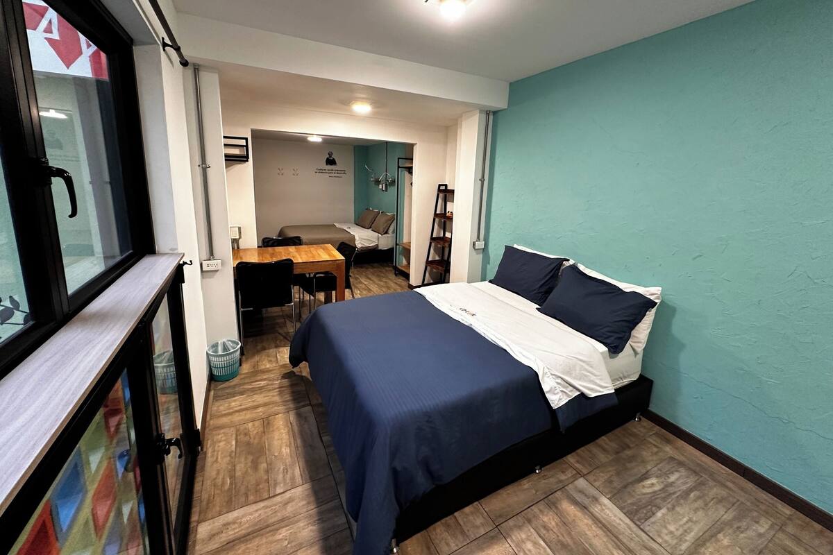 Ein Schlafzimmer mit Bett, Schreibtisch und Stuhl. Ein Fenster bietet Blick ins Freie.