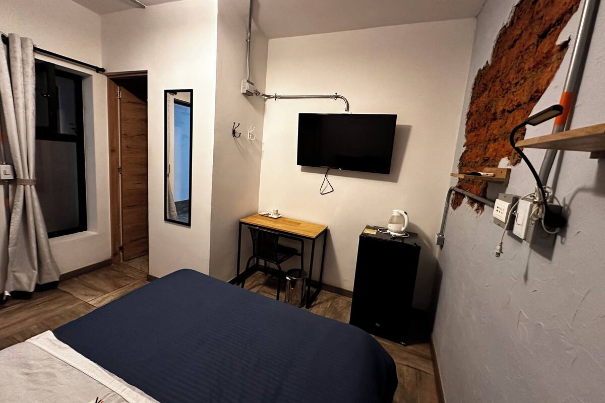 Ein Schlafzimmer mit Bett, Schreibtisch, Stuhl, Fernseher und einer Ziegelwand.