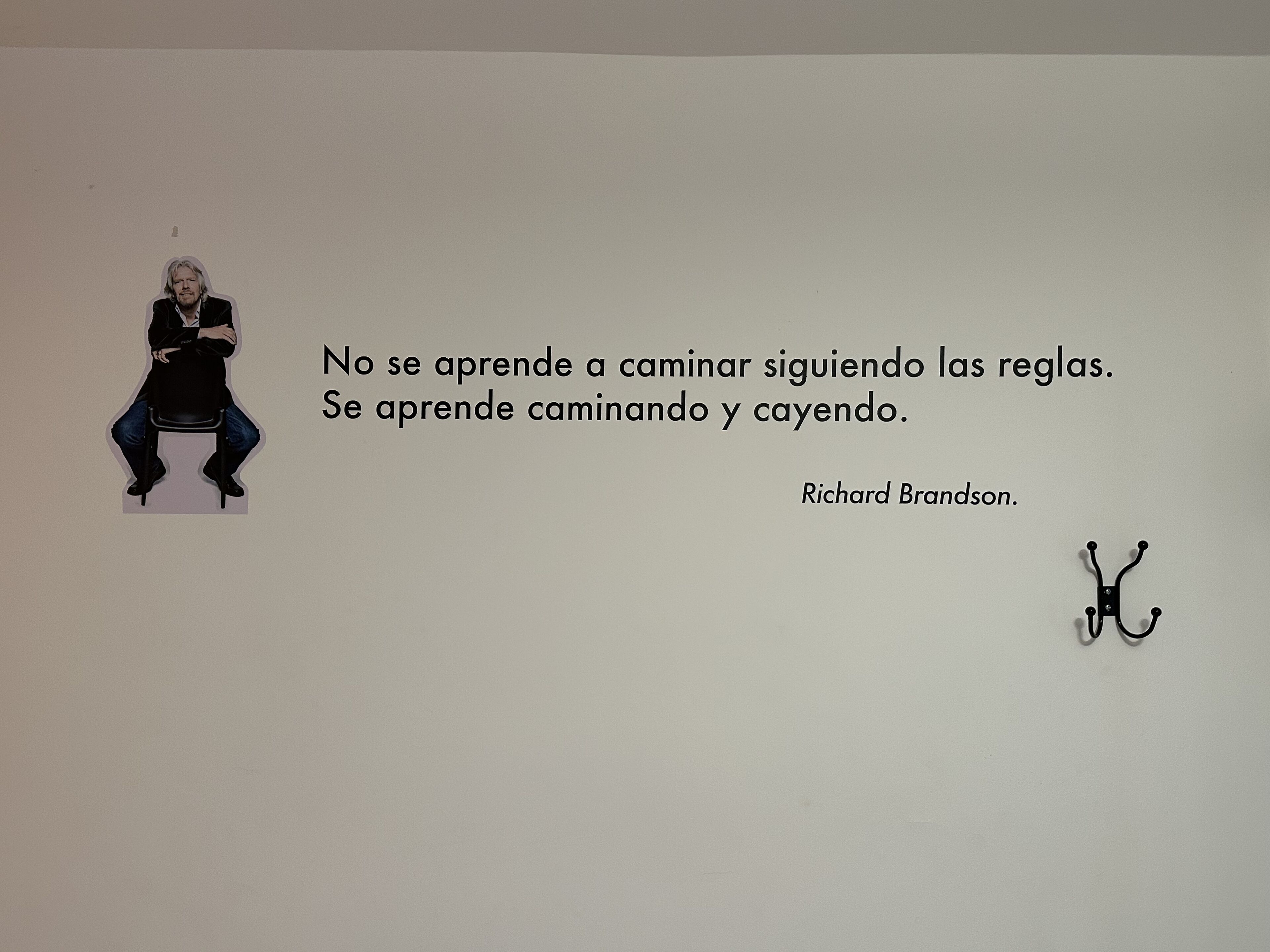 A wall with a quote by Richard Branson and a black coat hanger.