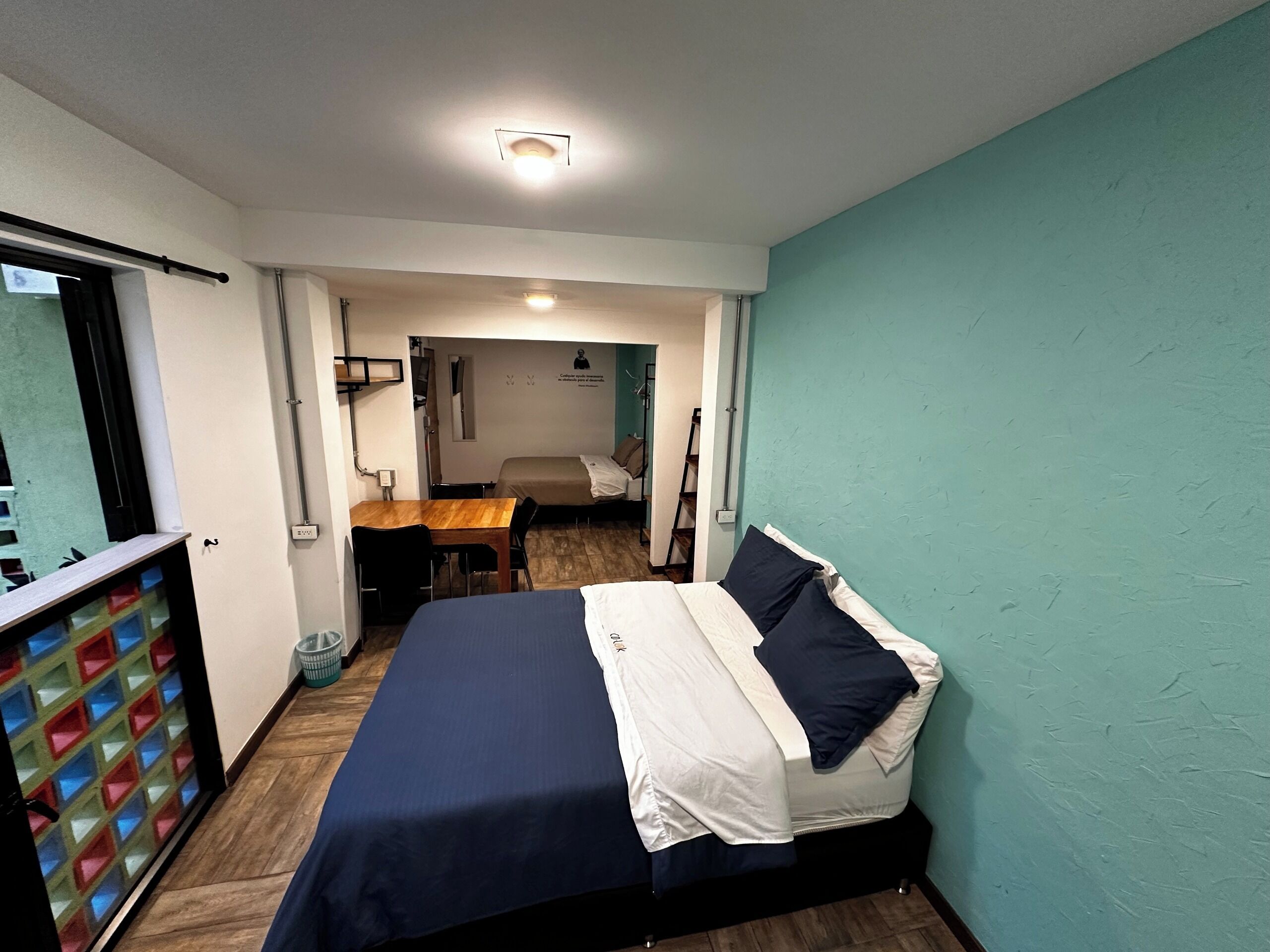 A bedroom with a bed, a desk, and a chair. There is a window with a view of the outside.