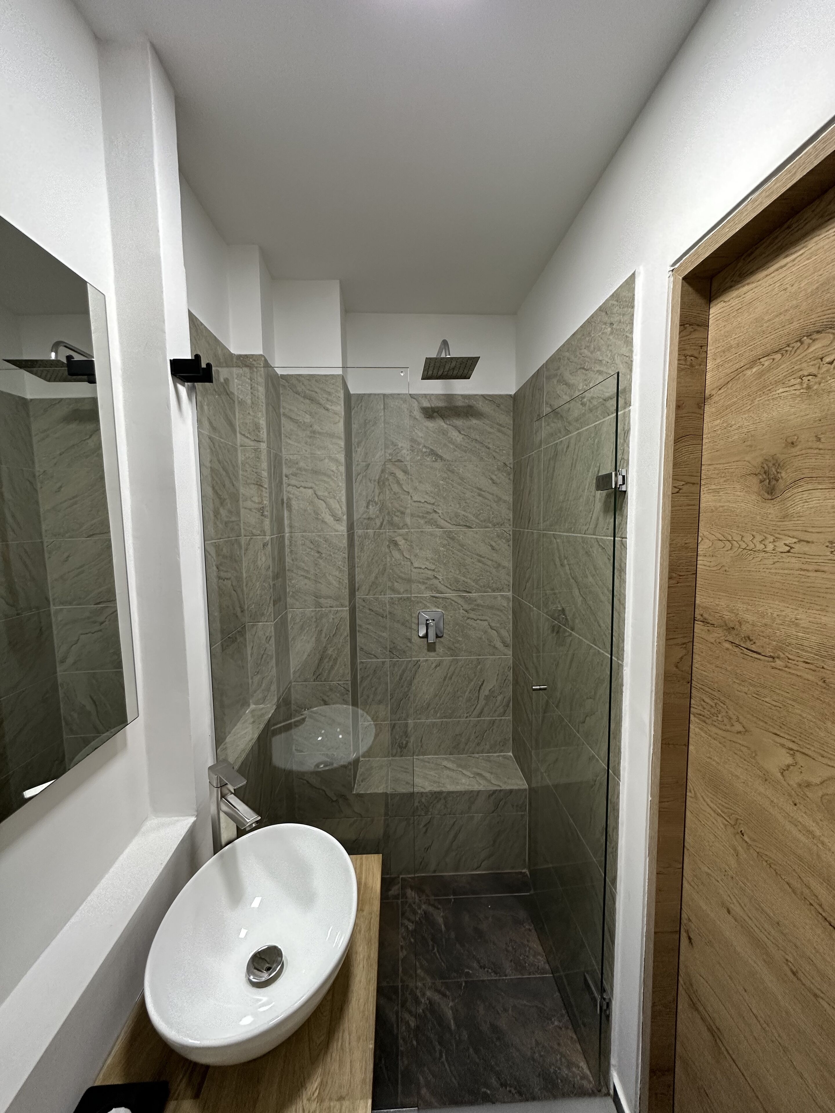 Un baño con lavamanos blanco, cabina de ducha de vidrio y tocador de madera.