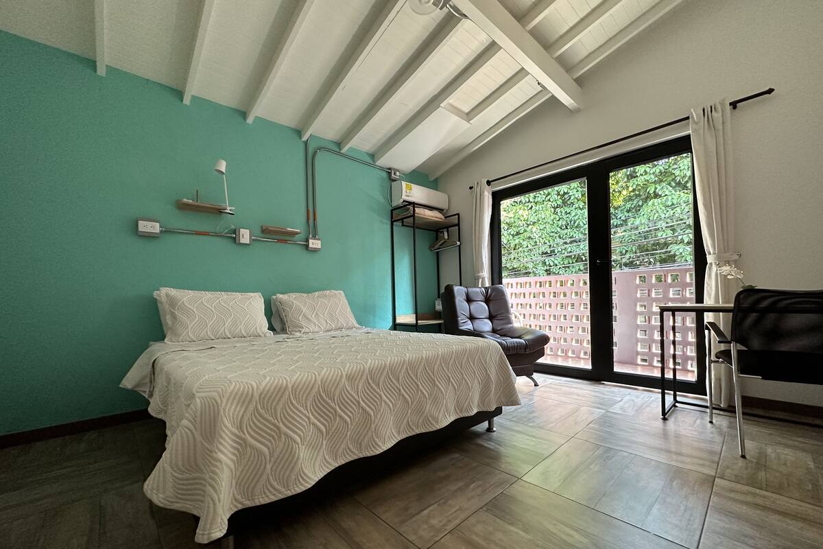 Ein Schlafzimmer mit Bett, Stuhl und einem Fenster mit Blick auf Grünflächen.