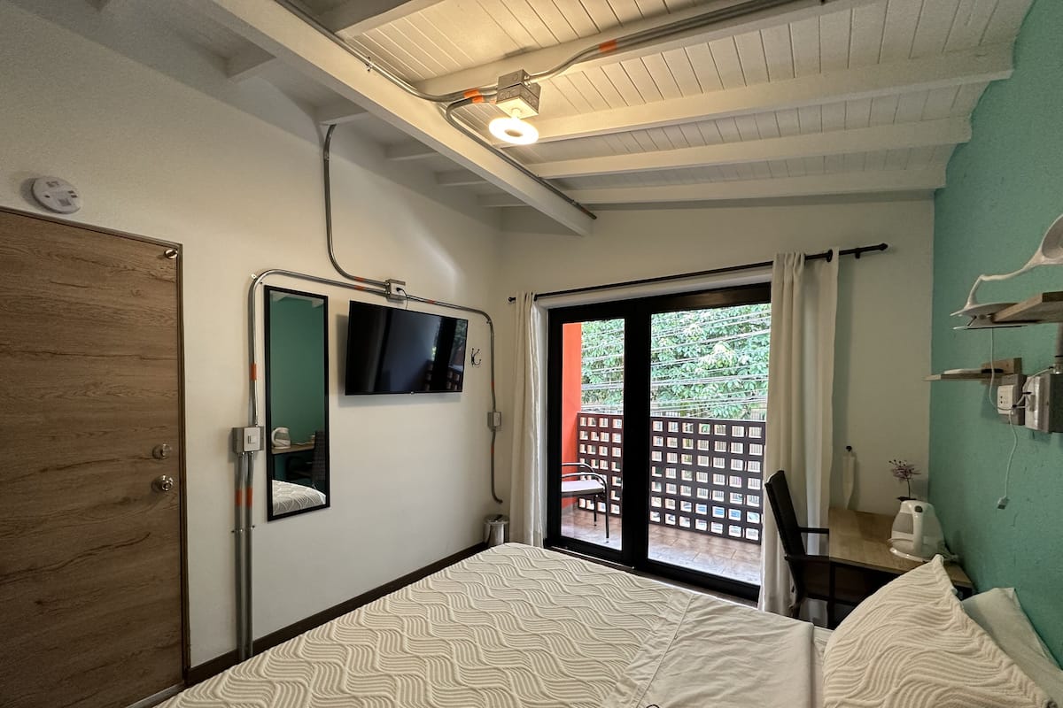 Ein Schlafzimmer mit einem Bett, einem Fernseher, einer Holztür und einer Schiebeglastür, die zu einem Außenbereich führt.
