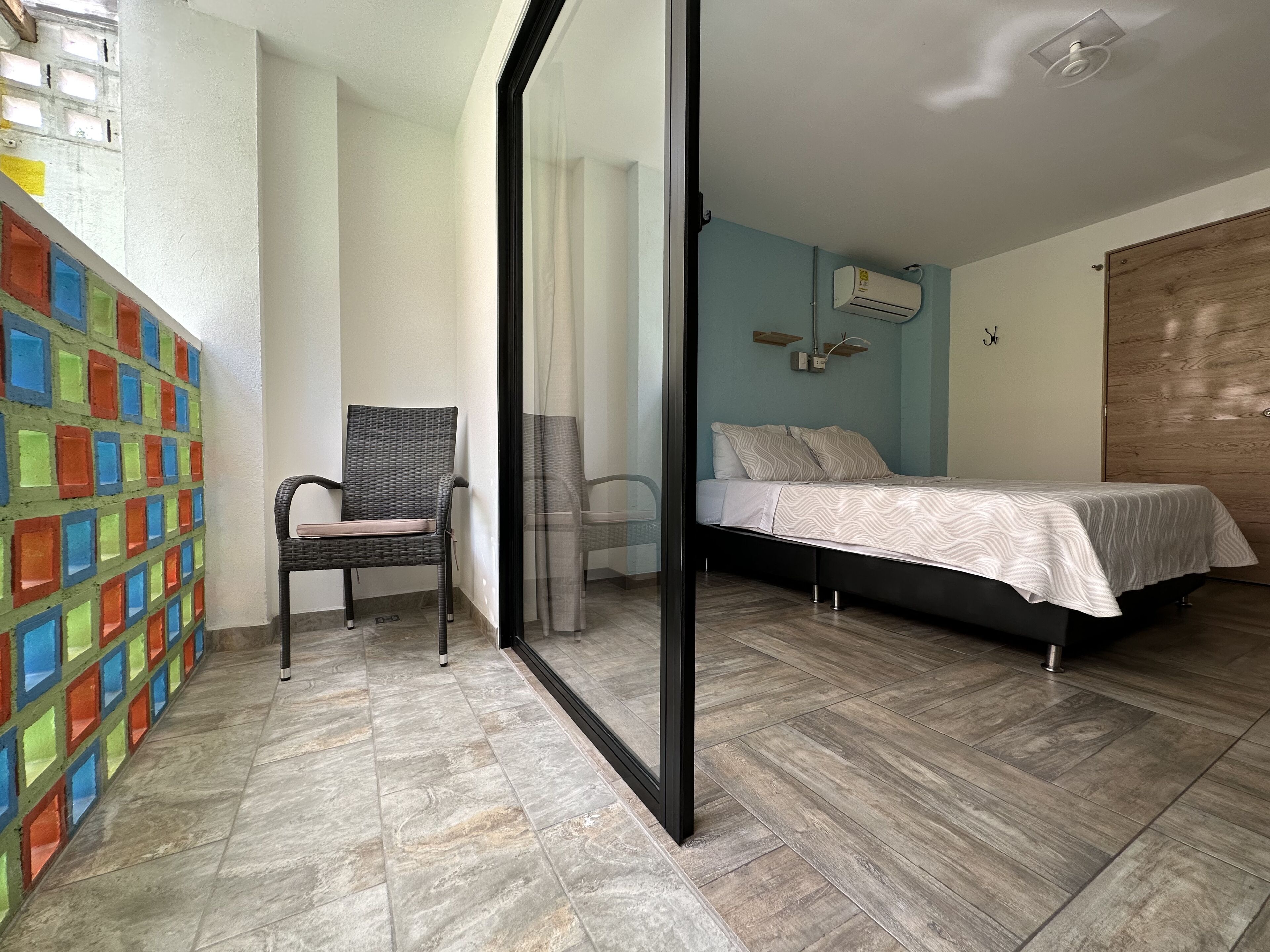 A bedroom with a bed, a chair, a colorful wall, and a window.