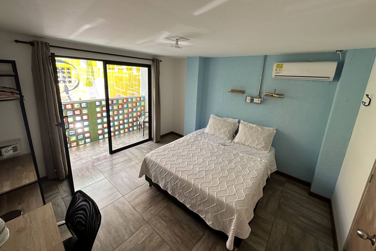 Ein Schlafzimmer mit einem Bett, einem Sessel, einem Schreibtisch und einer Glastür zum Balkon.
