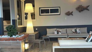 Ein modernes Wohnzimmer mit einer Couch, einem Couchtisch und einer Lampe. Es gibt ein kleines Fenster und ein an der Wand befestigtes Regal mit Dekoration.