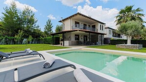 Ein zweigeschossiges Haus mit Swimmingpool, Gartenmöbeln und einem gepflegten Rasen.