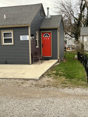 A guest house with a red door, a 'Guest House' sign, and a small porch with chairs. - Port Clinton Cozy Cottage (Port Clinton)