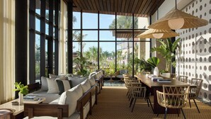 Un espacio interior amplio con un gran ventanal, techo de madera y una zona de comedor con sillas de mimbre y una mesa.