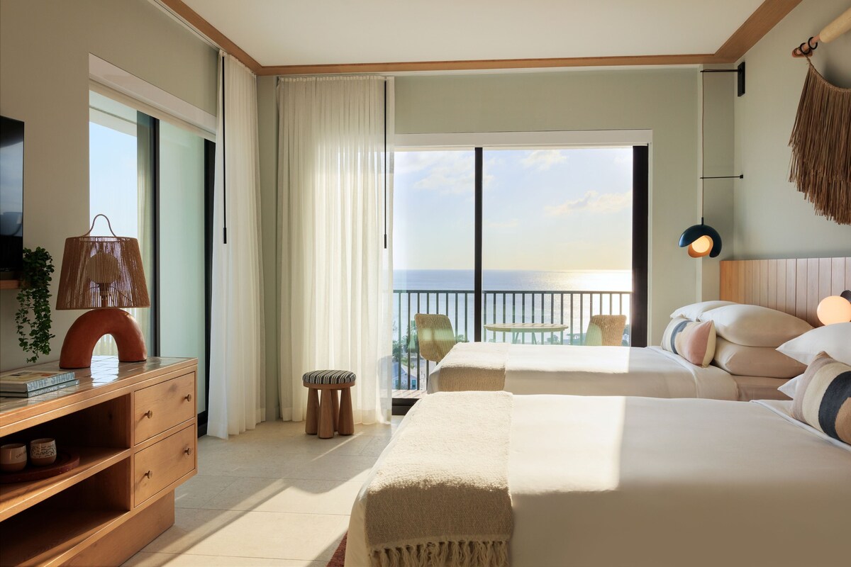 Habitación de hotel con balcón, televisor, escritorio y dos camas.