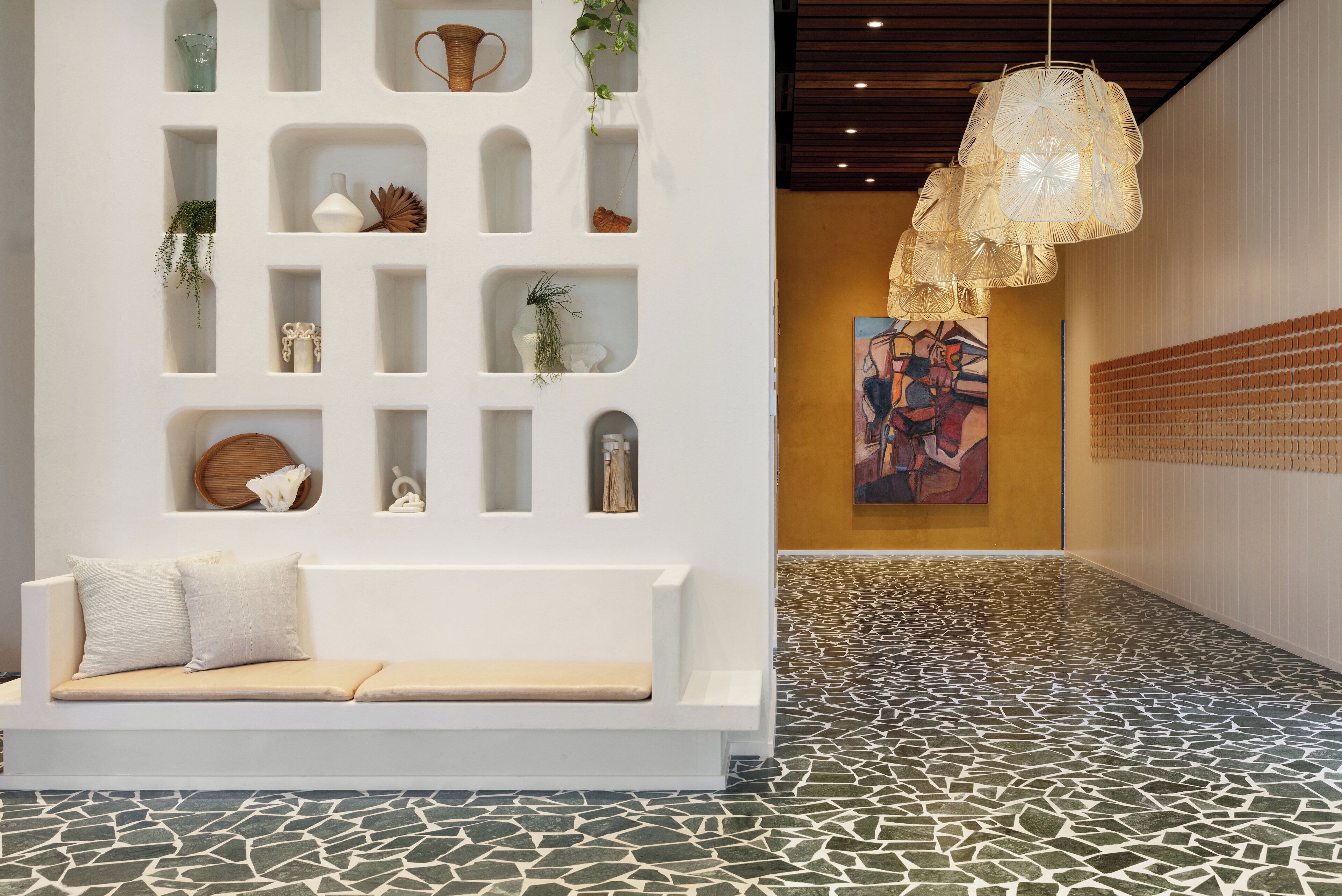 A modern interior with a white bench, a wall with shelves, and a patterned floor.
