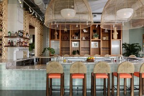 A bar area with wicker chairs, a bar counter, and shelves with bottles and glasses.