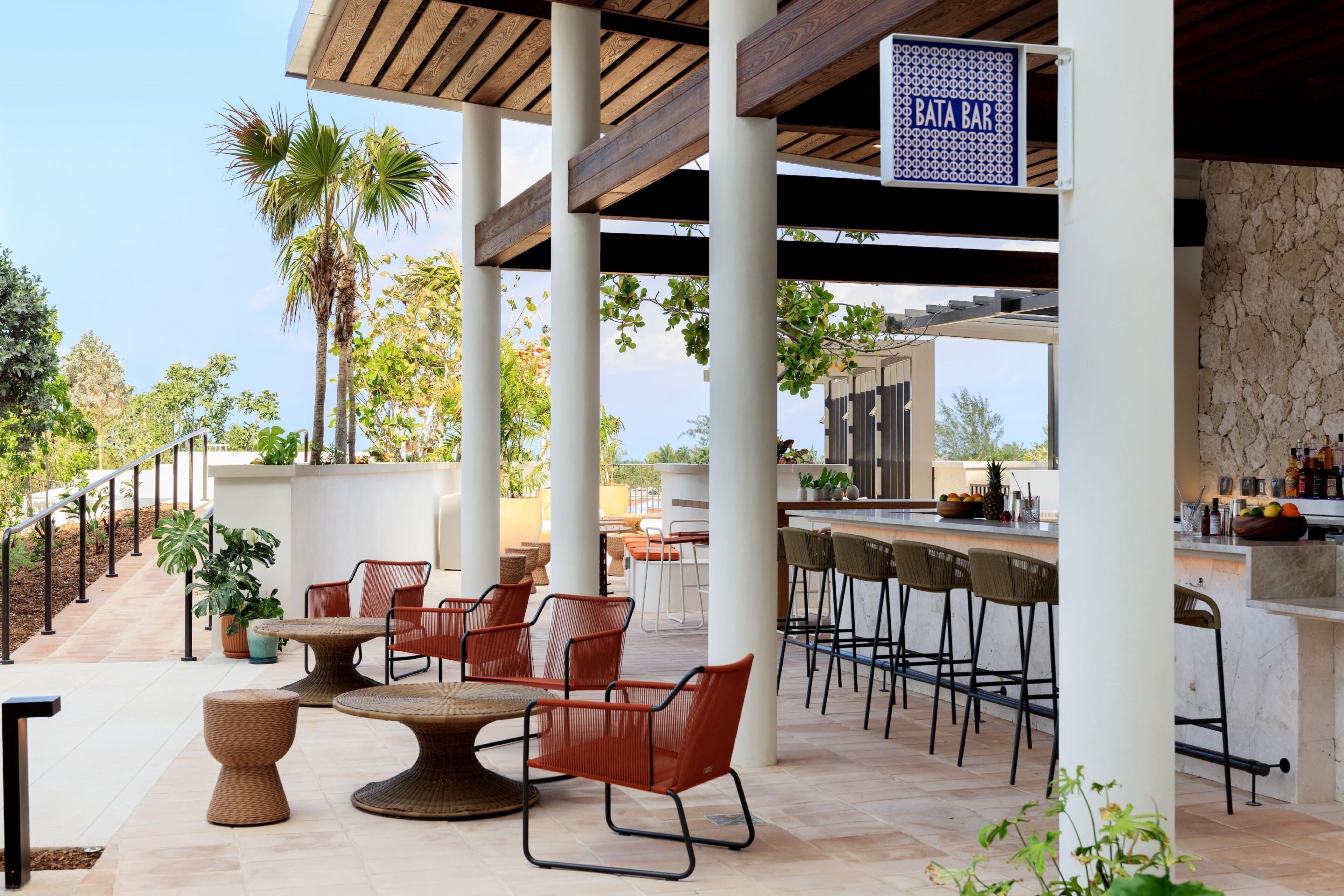 An outdoor bar area with high stools, a round table, and potted plants.