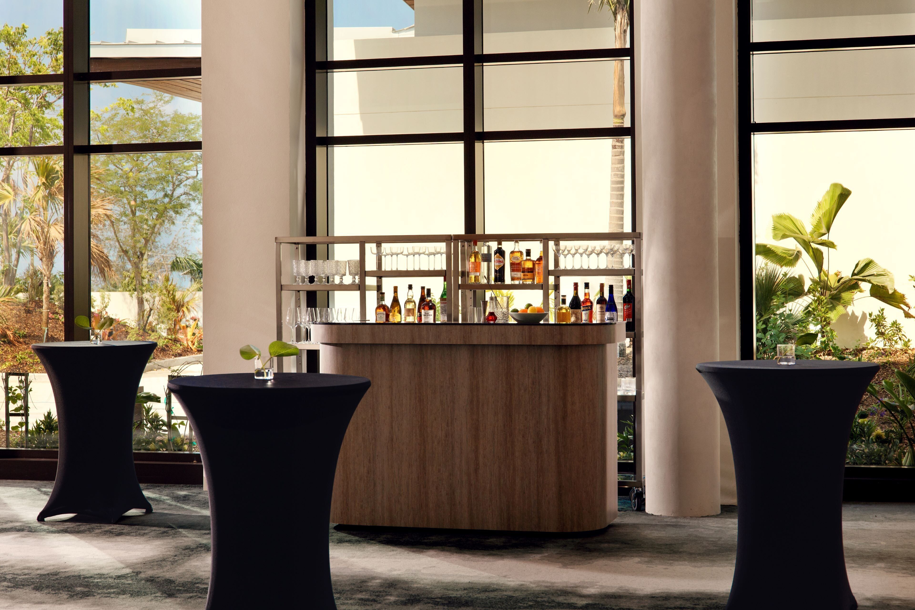 A bar area with a wooden counter, surrounded by large windows and two black tables.