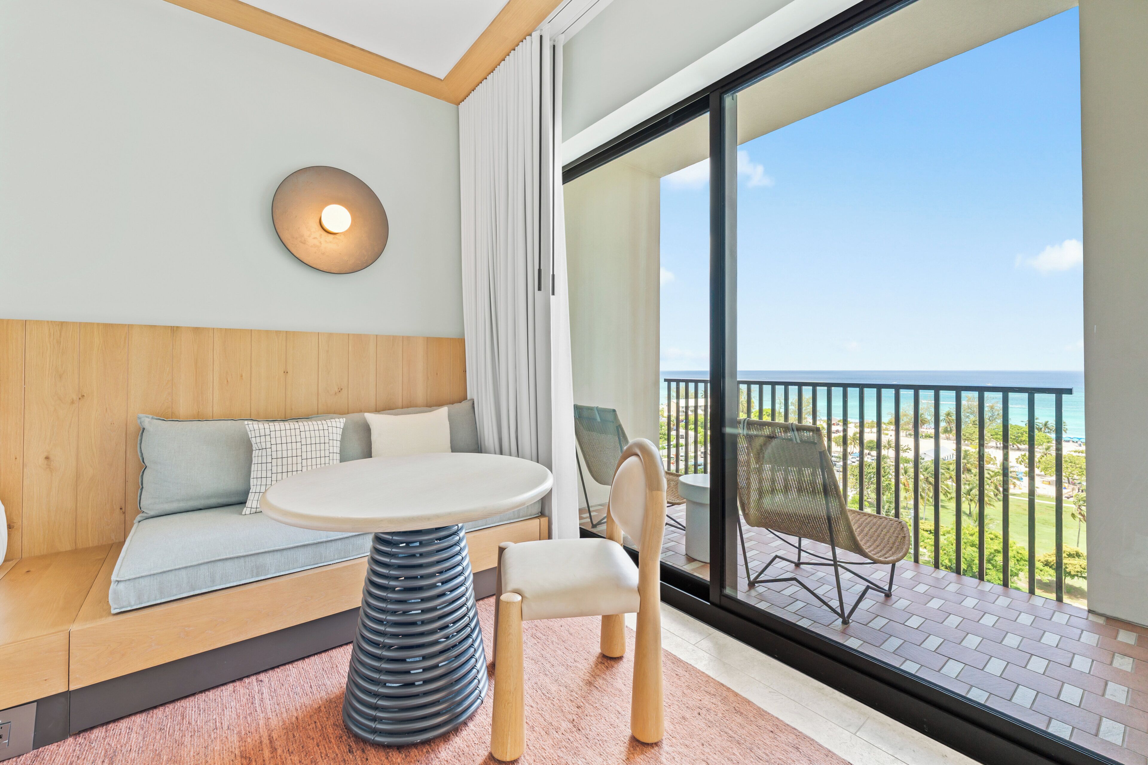 Een moderne kamer met een ronde tafel, een bank en een balkon met uitzicht op zee.