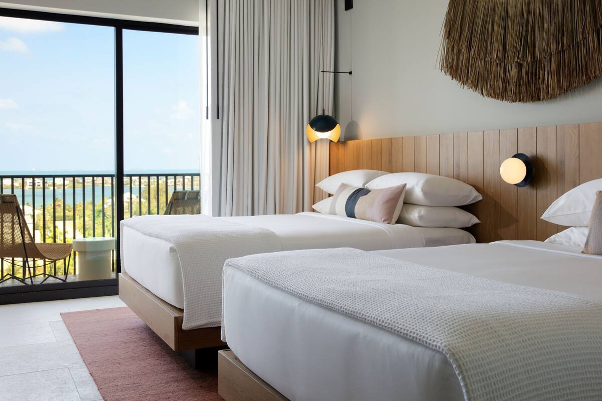 A hotel room with two beds, a balcony with a view, and a woven wall hanging.