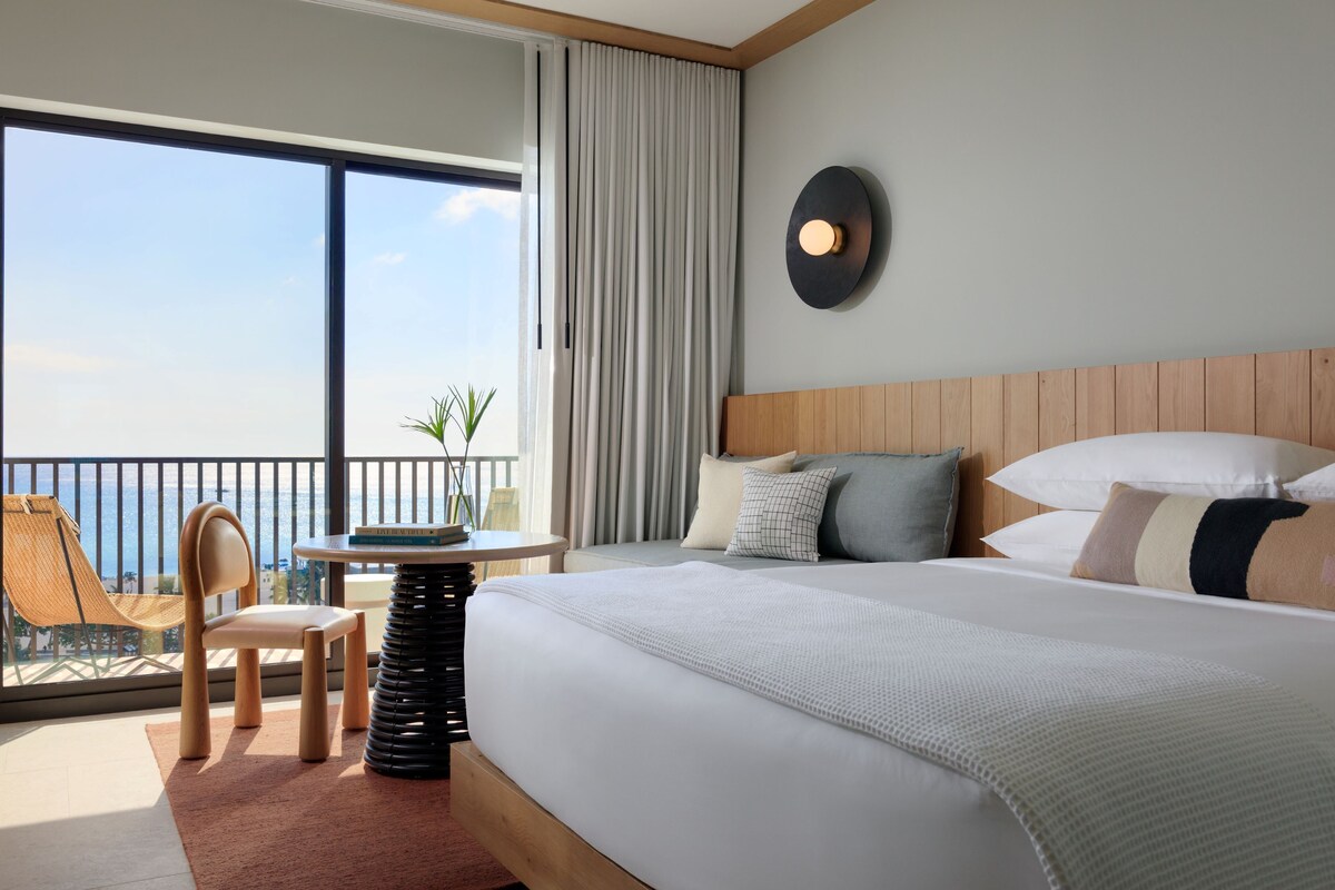 Habitación de hotel con una cama grande, una mesa redonda, una silla y vista al océano.