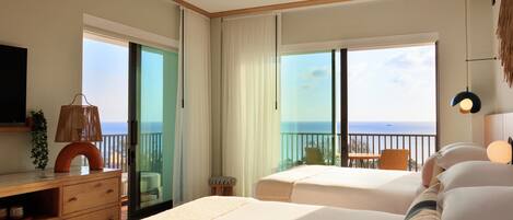A hotel room with two beds, a wooden dresser, a TV, and a balcony with a view of the ocean.