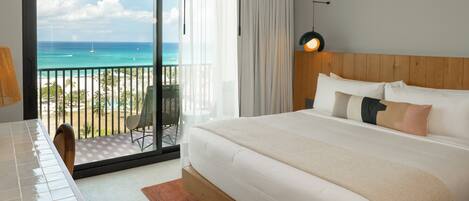 A hotel room with a large bed, a view of the beach and ocean, a balcony with a chair, and a table.