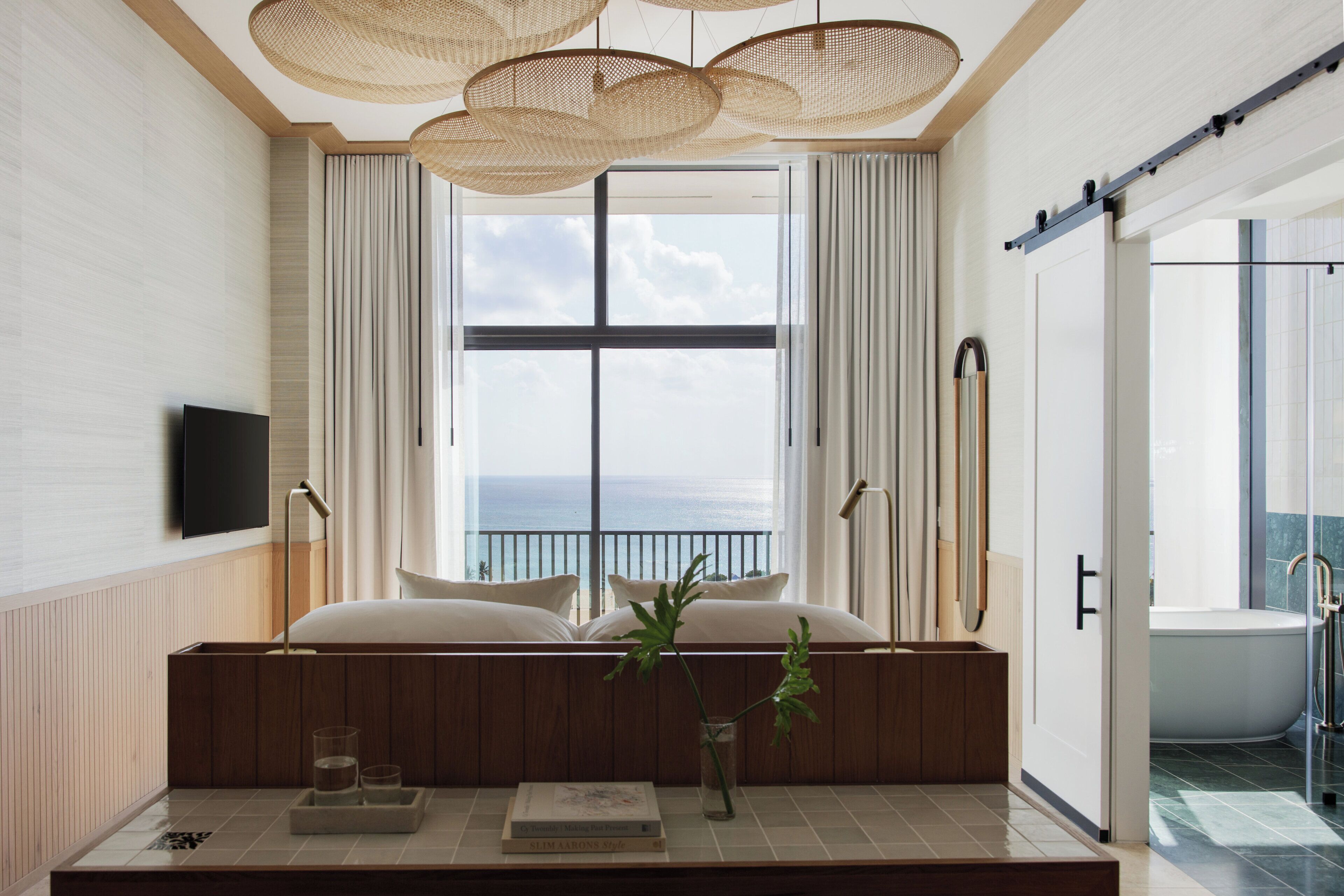 A modern bathroom with a bathtub, a shower, and a large window with a view of the sea.
