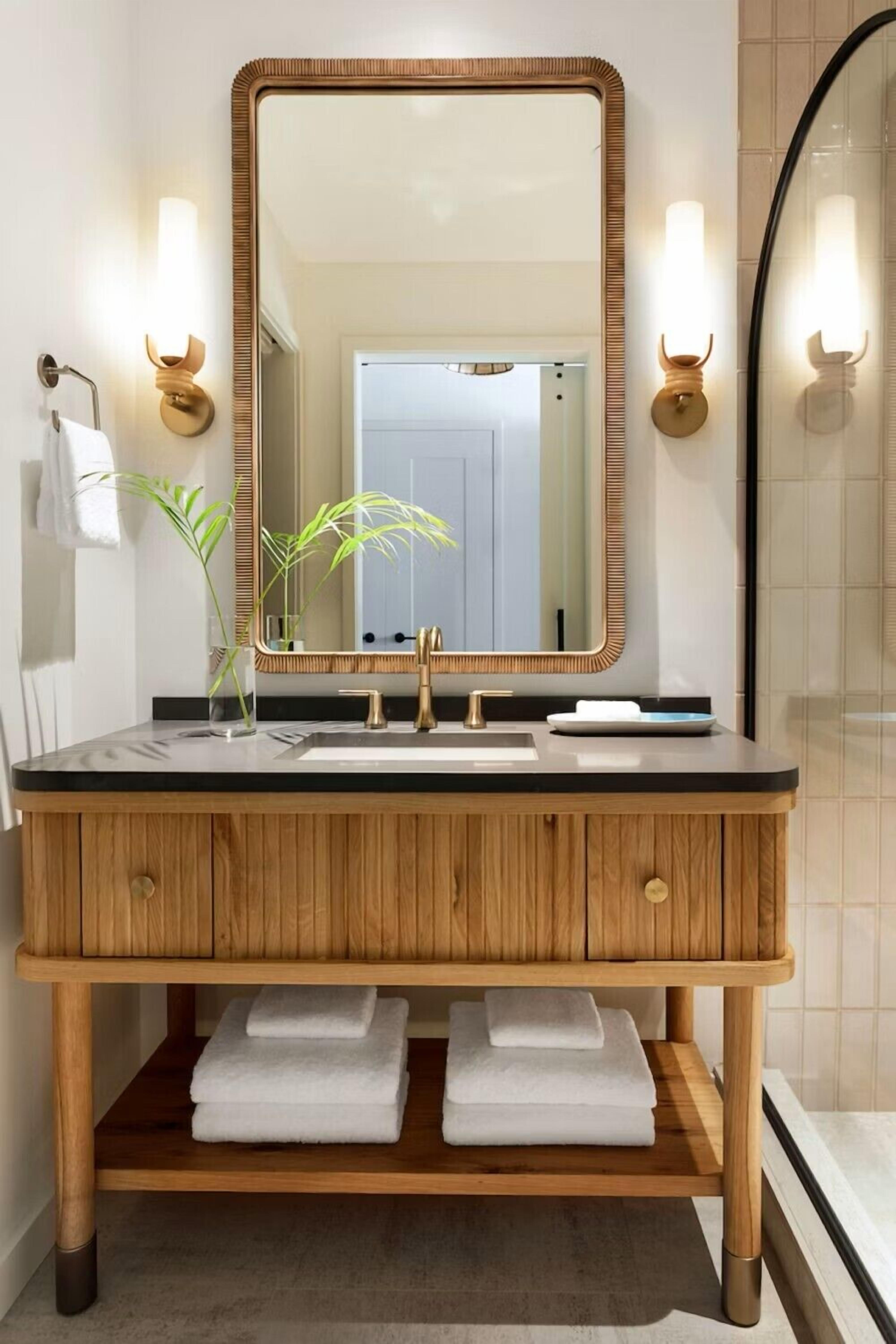 A wooden vanity with a large mirror, two wall-mounted lights, a sink, and a towel rack.