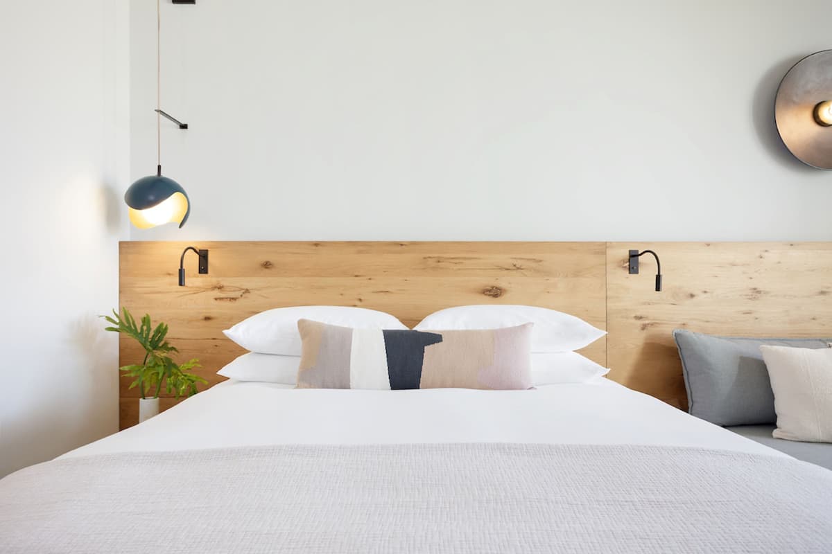 A neatly made bed with white linens, a wooden headboard, and two bedside lamps.