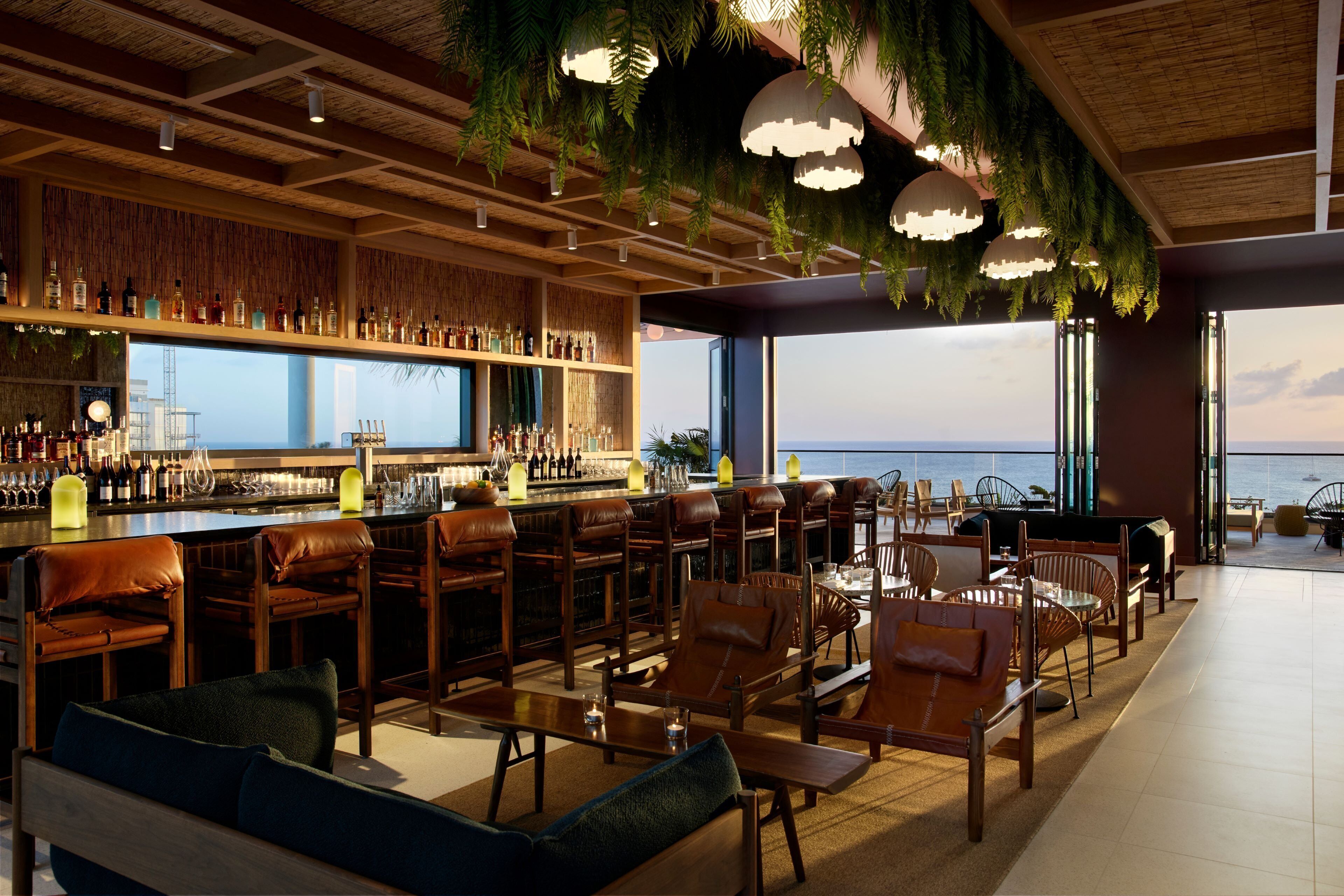 A bar area with a view of the ocean, wooden furniture, and hanging plants.