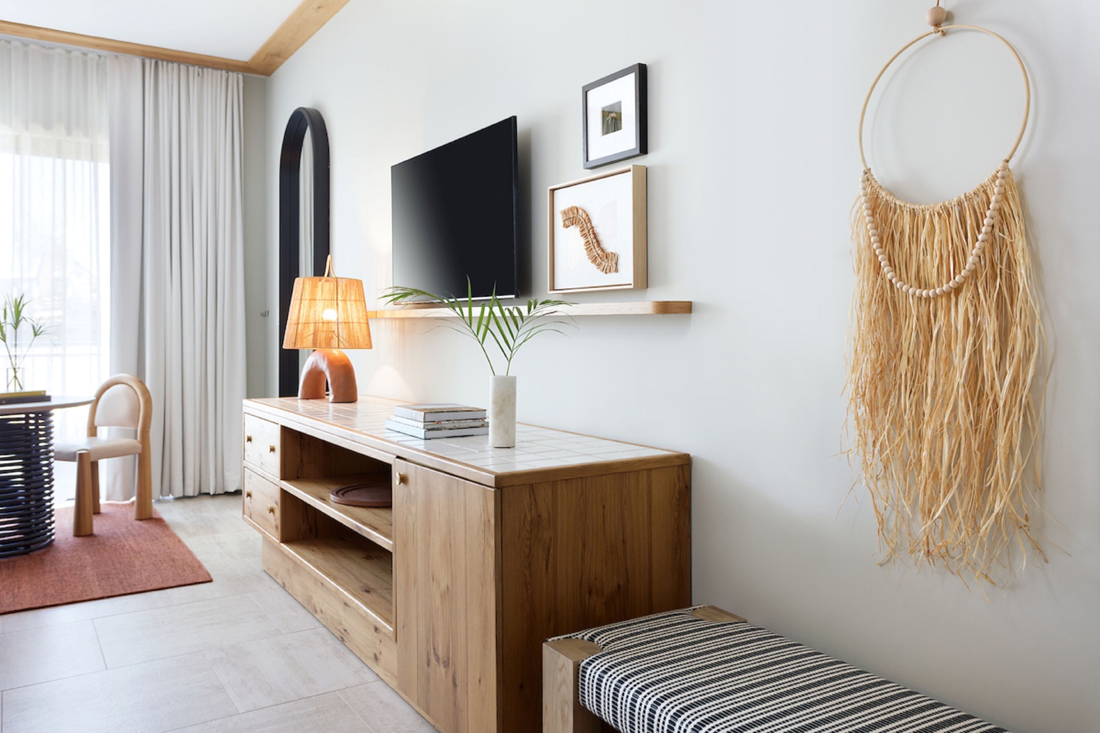Un salon moderne avec un meuble en bois, un téléviseur à écran plat, une décoration murale en macramé et un banc à rayures.
