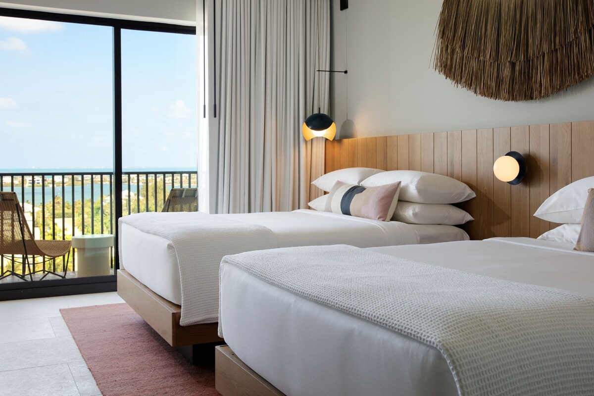 Habitación de hotel con dos camas, un balcón con vistas y un tapiz de pared tejido.